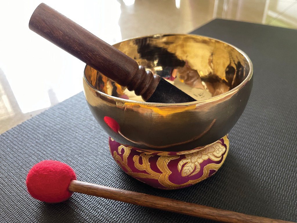 An AYA hand-hammered singing bowl on its cushion, with a wooden stick and a felt mallet